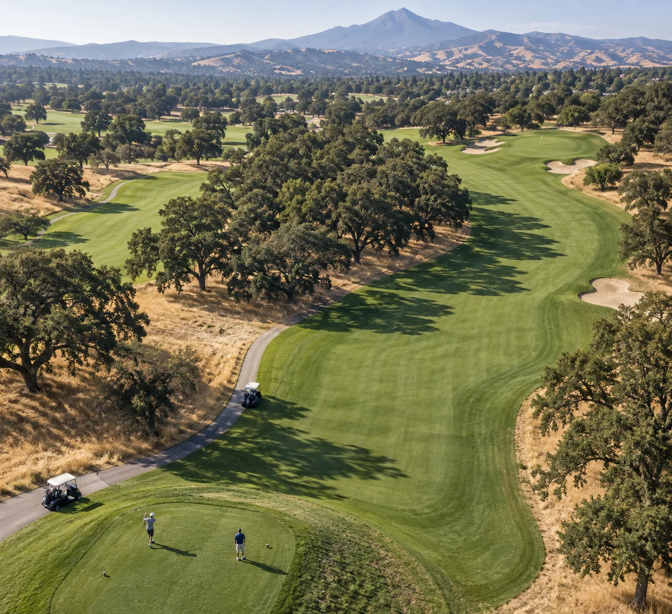 Aerial view of boundary oak golf course’s oak-lined dogleg fairway, golfers, carts, bunkers, and Mount Diablo foothills.