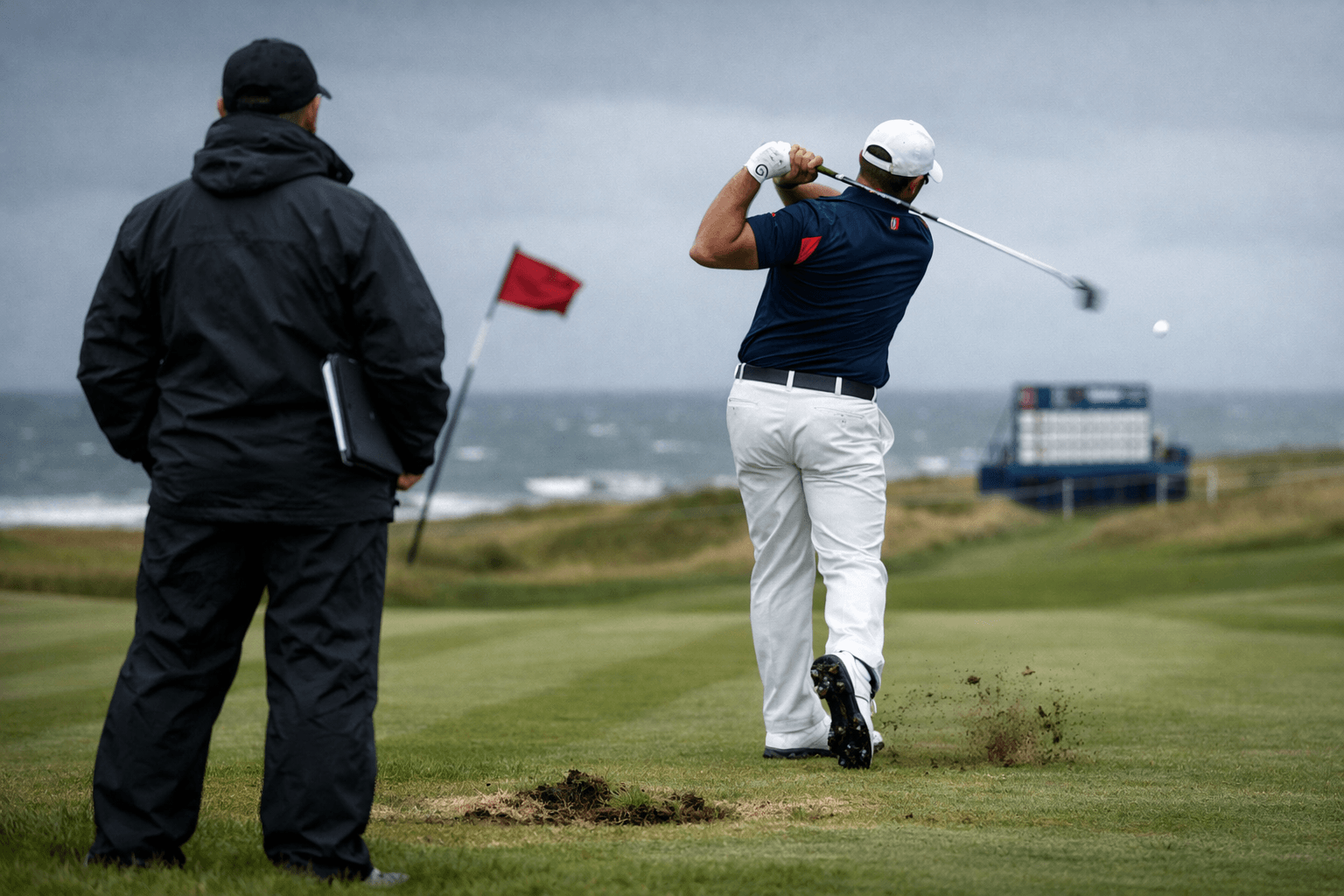 tommy fleetwood golfer swings on windy links as coach watches, ball lifting off