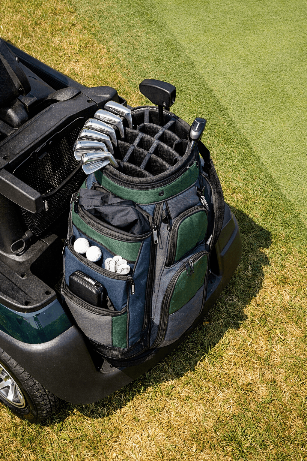 Overhead view of a golf cart with a golf bag in the rear rack on sunlit grass beside a fairway.
