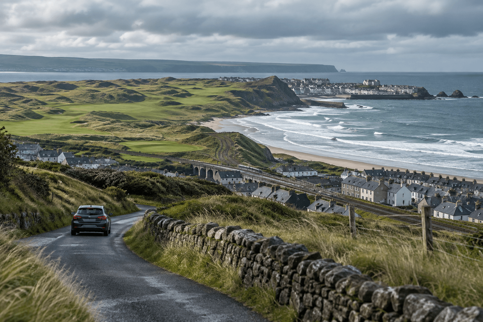 A rental car follows a coastal road toward Royal Portrush, with rolling golf-course dunes and the Atlantic beyond.