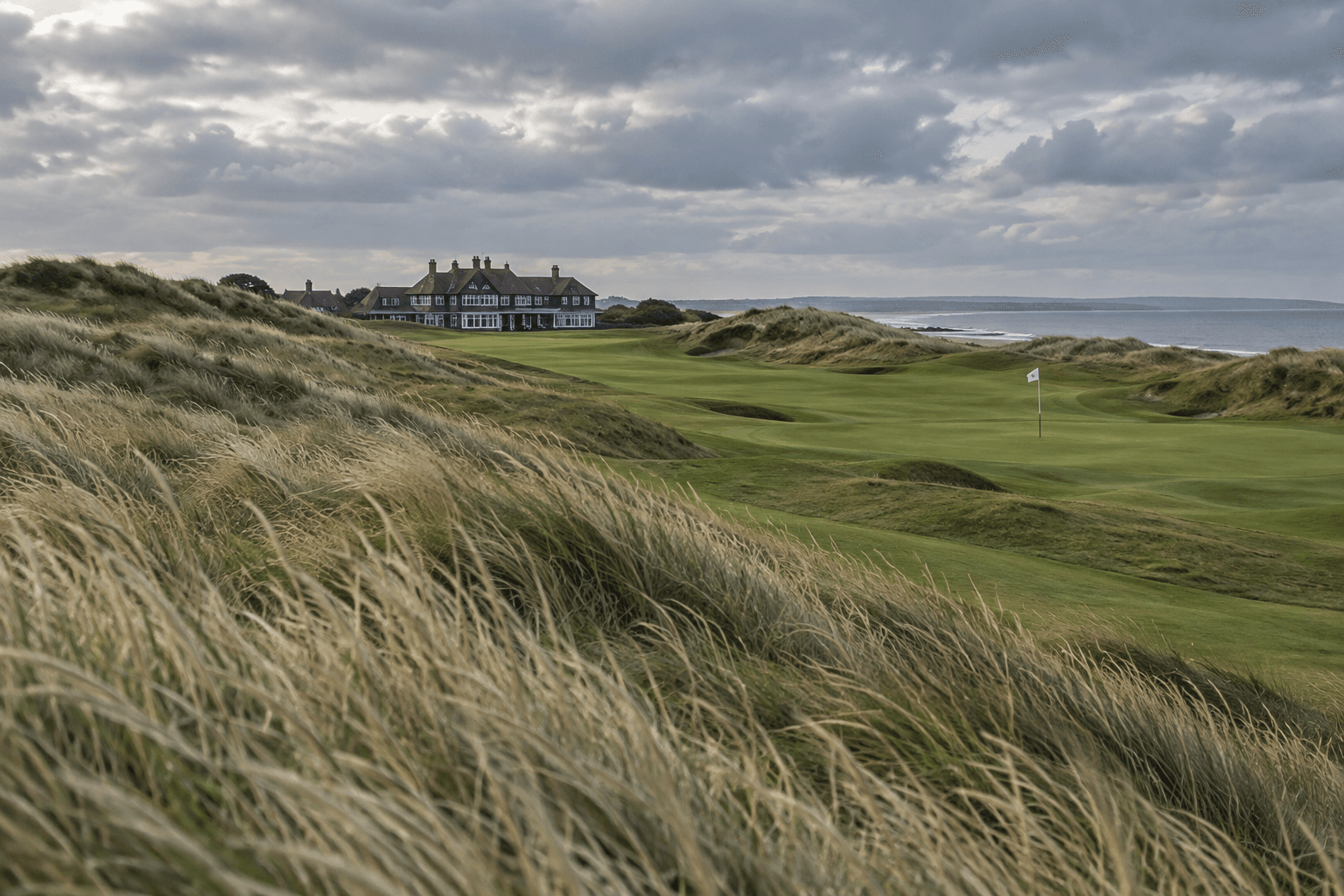 Royal Birkdale: Course Guide, History, and Visitor Tips 1 Royal Birkdaleu2019s rolling links course winds between golden dunes toward the clubhouse, with a flag beneath a cloudy sky.